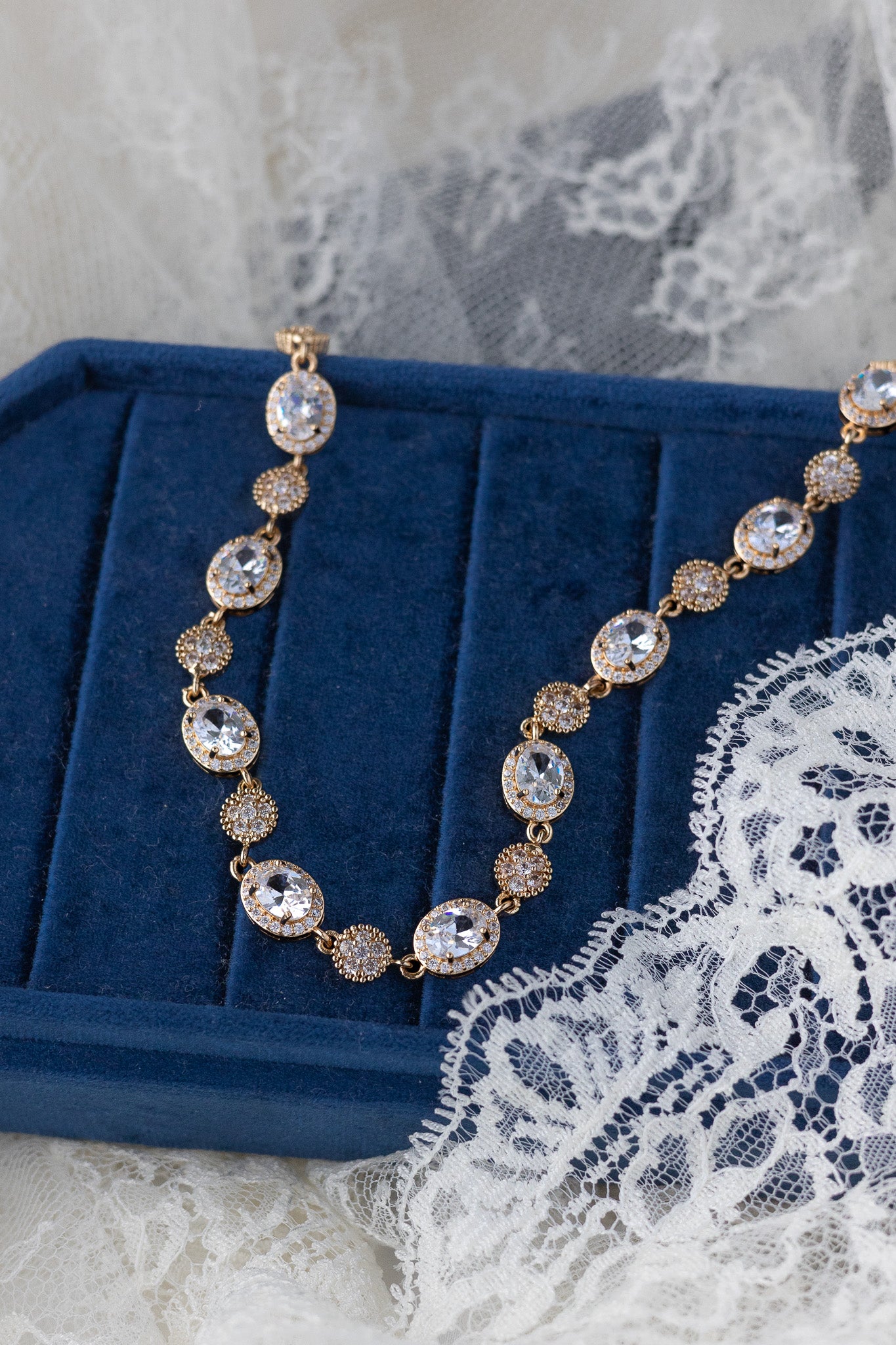 Gold necklace with crystals on a blue velvet stand with lace background
