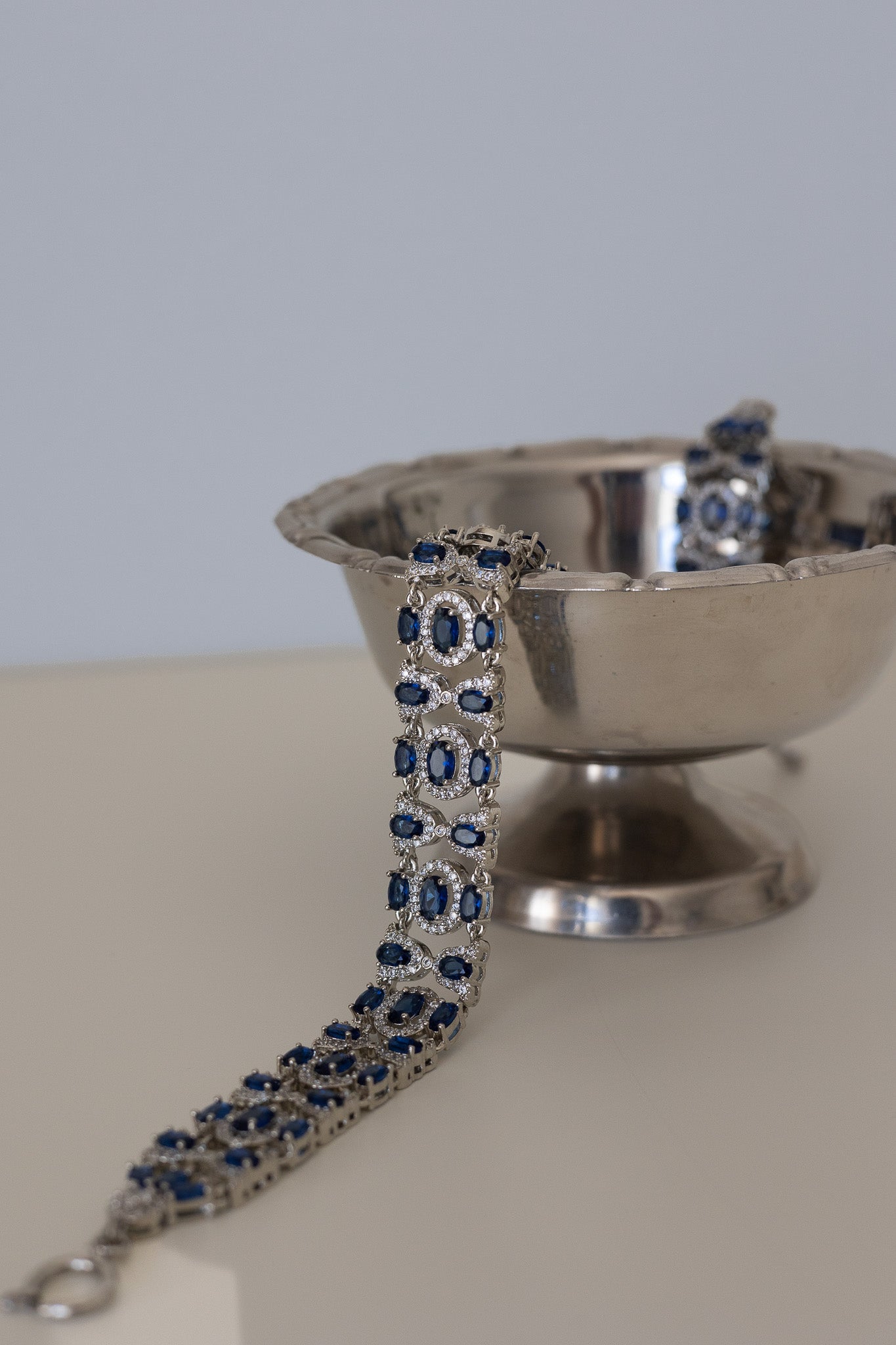 Silver necklace with blue stones on a stand against a neutral background