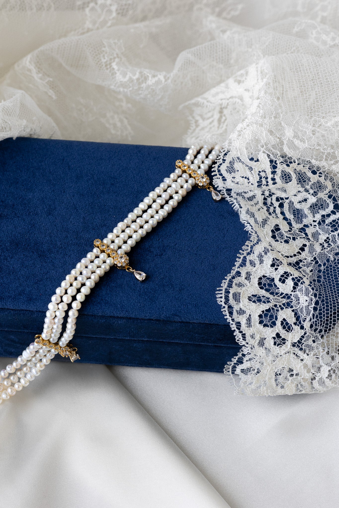 Pearl necklace with gold clasp on a blue box with lace detailing