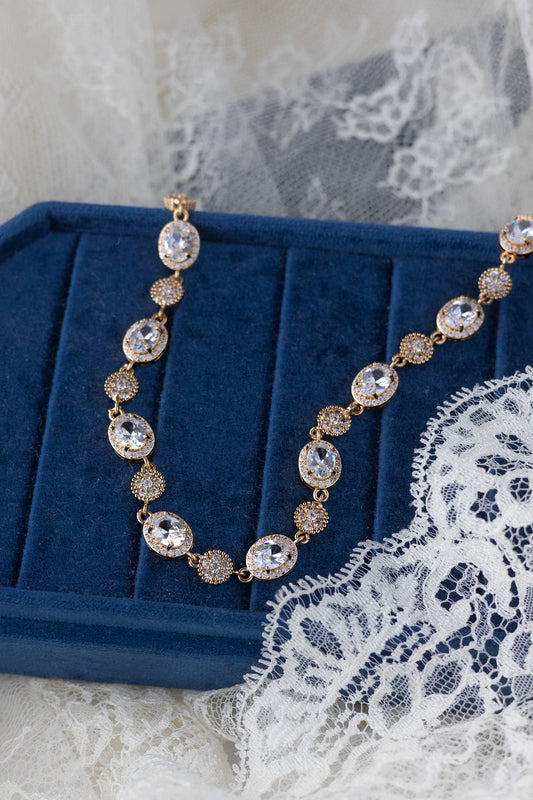 Gold necklace with crystals on a blue velvet stand with lace background