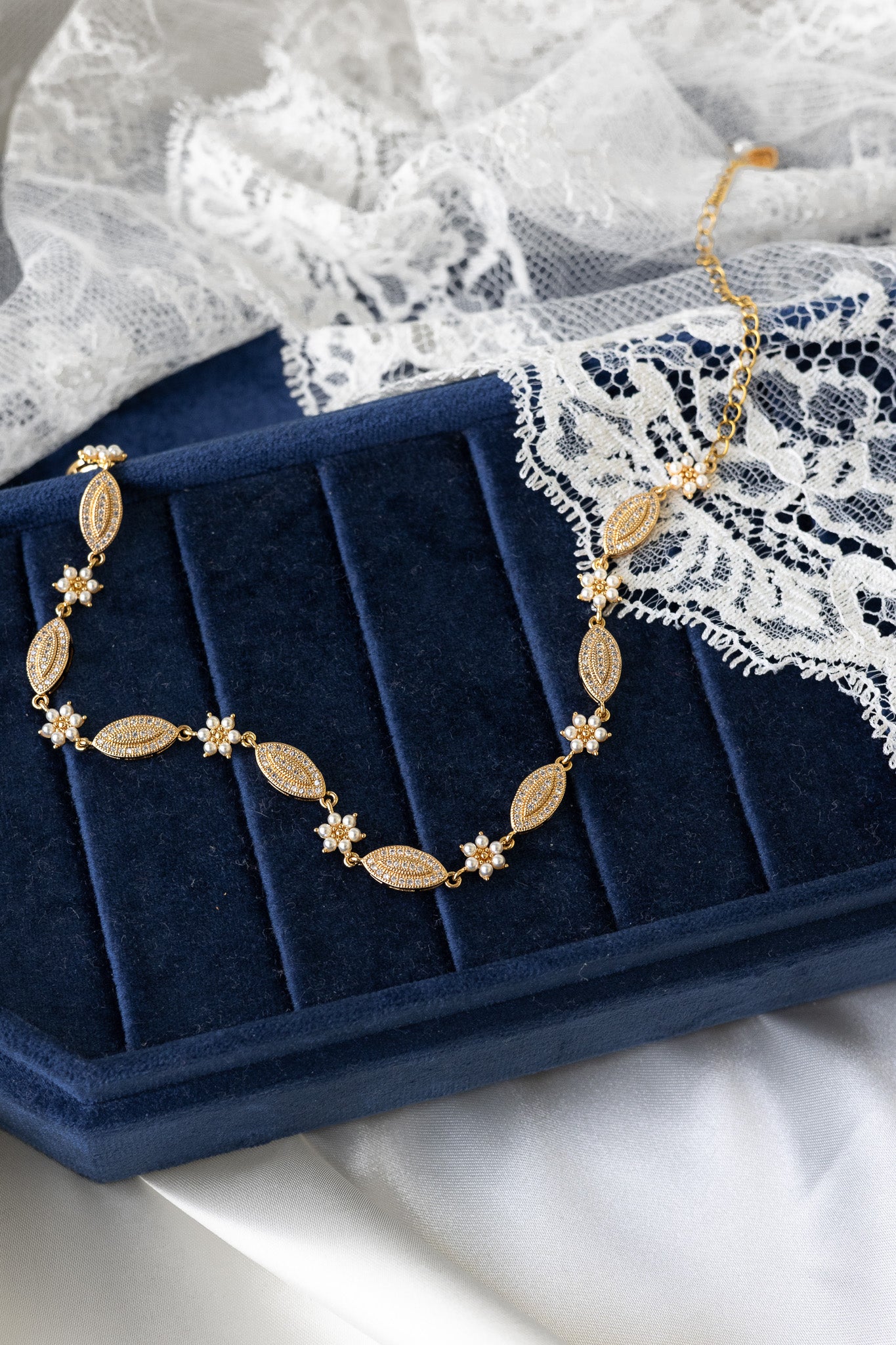 Gold necklace on a blue jewelry box with lace fabric in the background