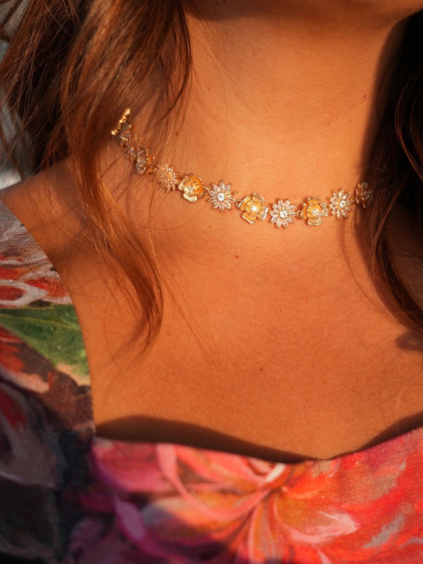 Close-up of a floral choker on a person with a colorful garment in the background