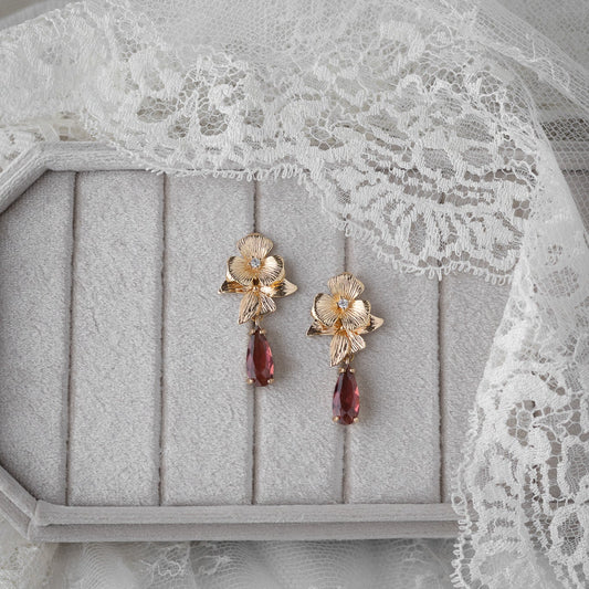 Gold floral earrings with garnet drops on a gray surface with lace fabric.