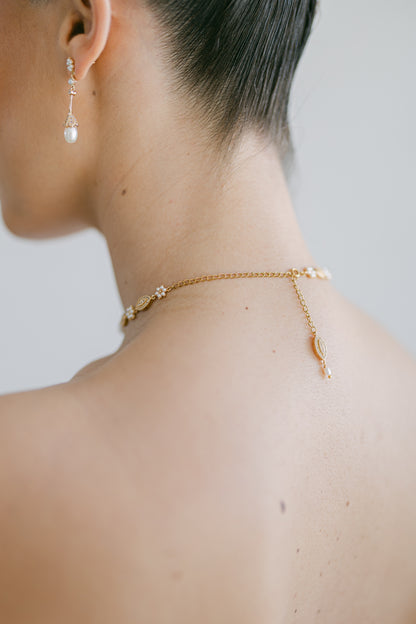 Close-up of a person wearing a gold necklace and earrings against a neutral background