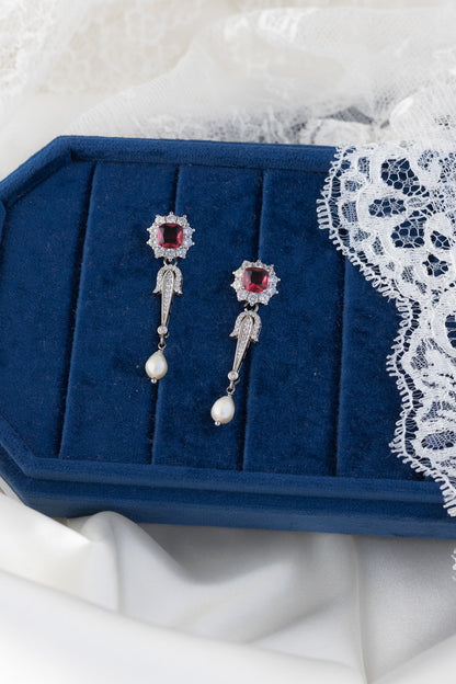 Pair of silver earrings with red gemstones on a blue jewelry box with lace trim.