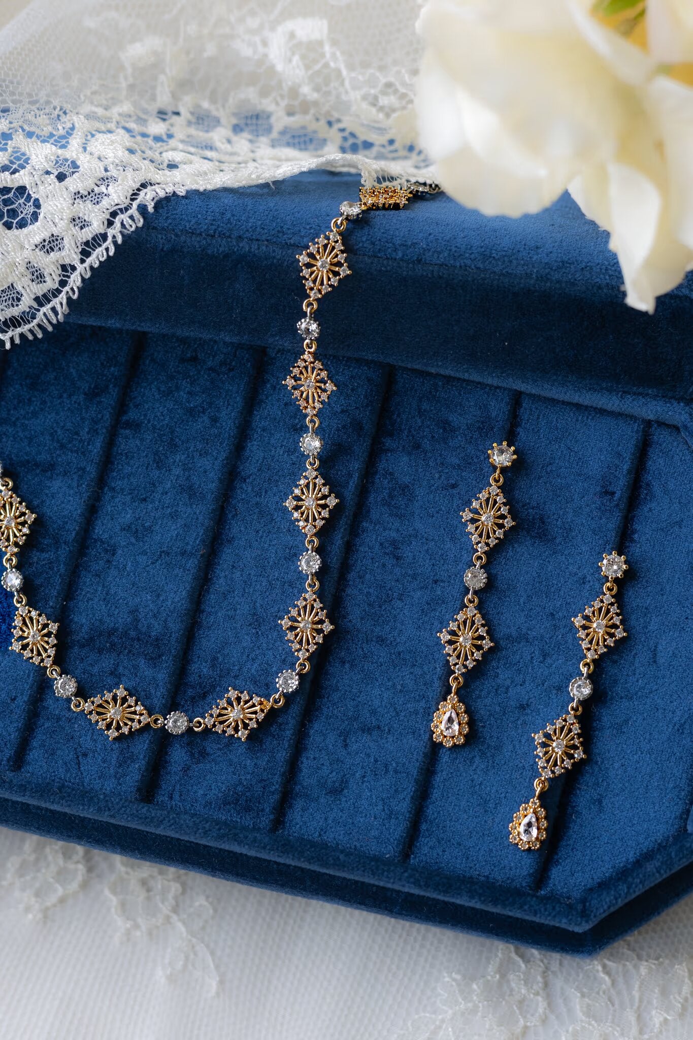Gold necklace and earrings on a blue jewelry box with lace and flowers in the background