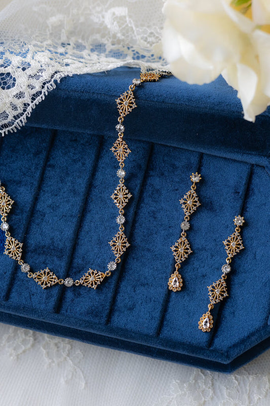 Gold necklace and earrings on a blue jewelry box with lace and flowers in the background