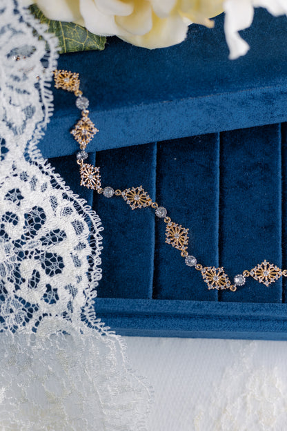 Gold necklace with geometric designs on a blue jewelry box with lace and flowers in the background