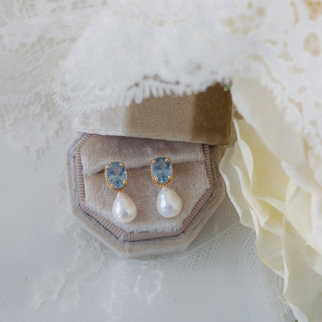 Pearl and gemstone earrings in a jewelry box on a textured white fabric background