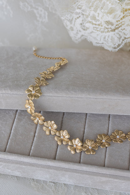 Gold floral necklace on a gray textured surface with lace in the background