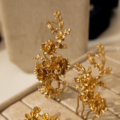 Gold floral earrings on a beige jewelry box