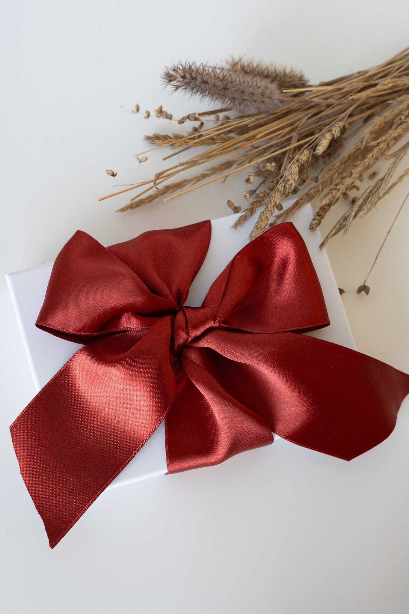Red satin bow on a white box with dried flowers on a light background