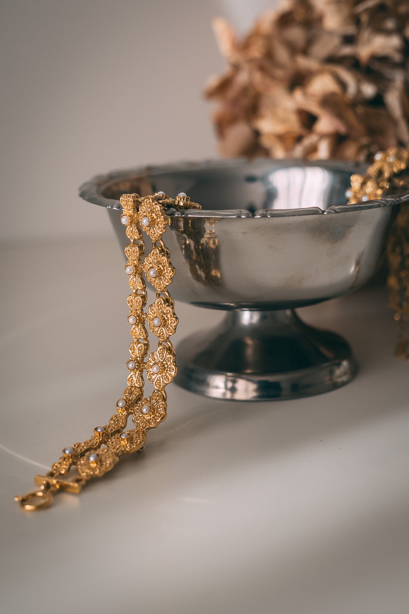 Decorative gold necklace on a silver bowl with a blurred natural background
