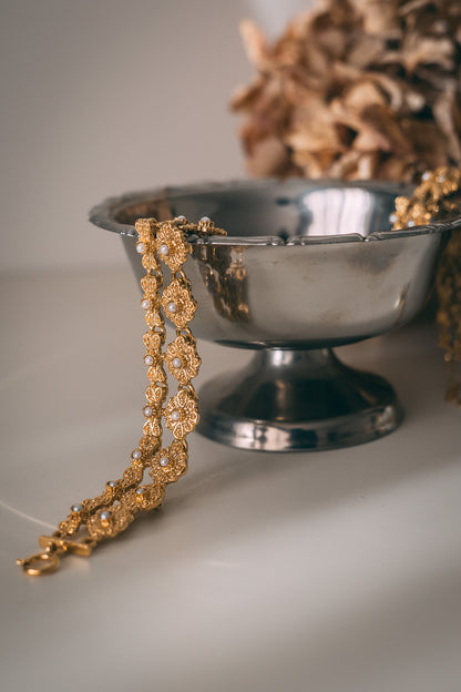 Decorative gold necklace on a silver bowl with a blurred natural background