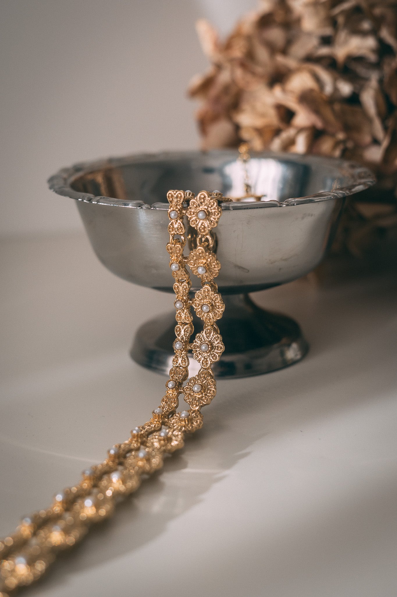 Gold vintage necklace draped over a silver bowl on a neutral background