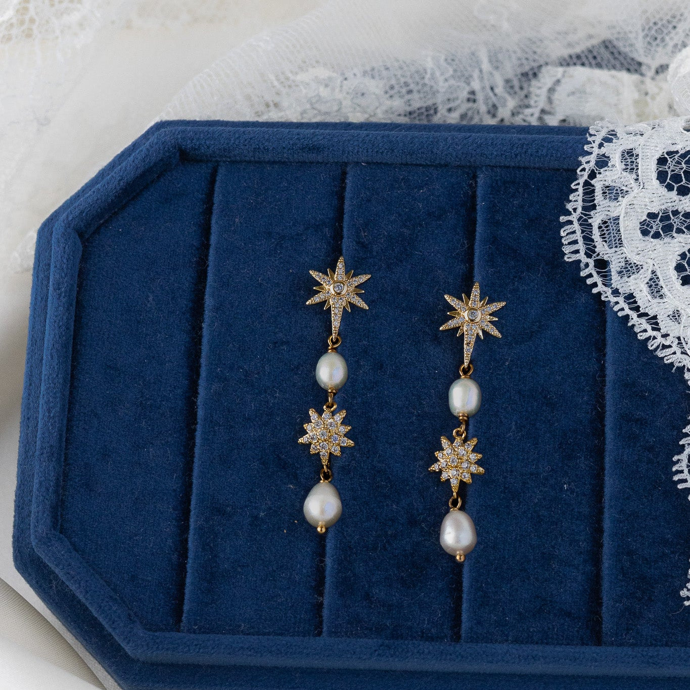 Pair of gold star-shaped earrings with pearl drops on a blue jewelry box.